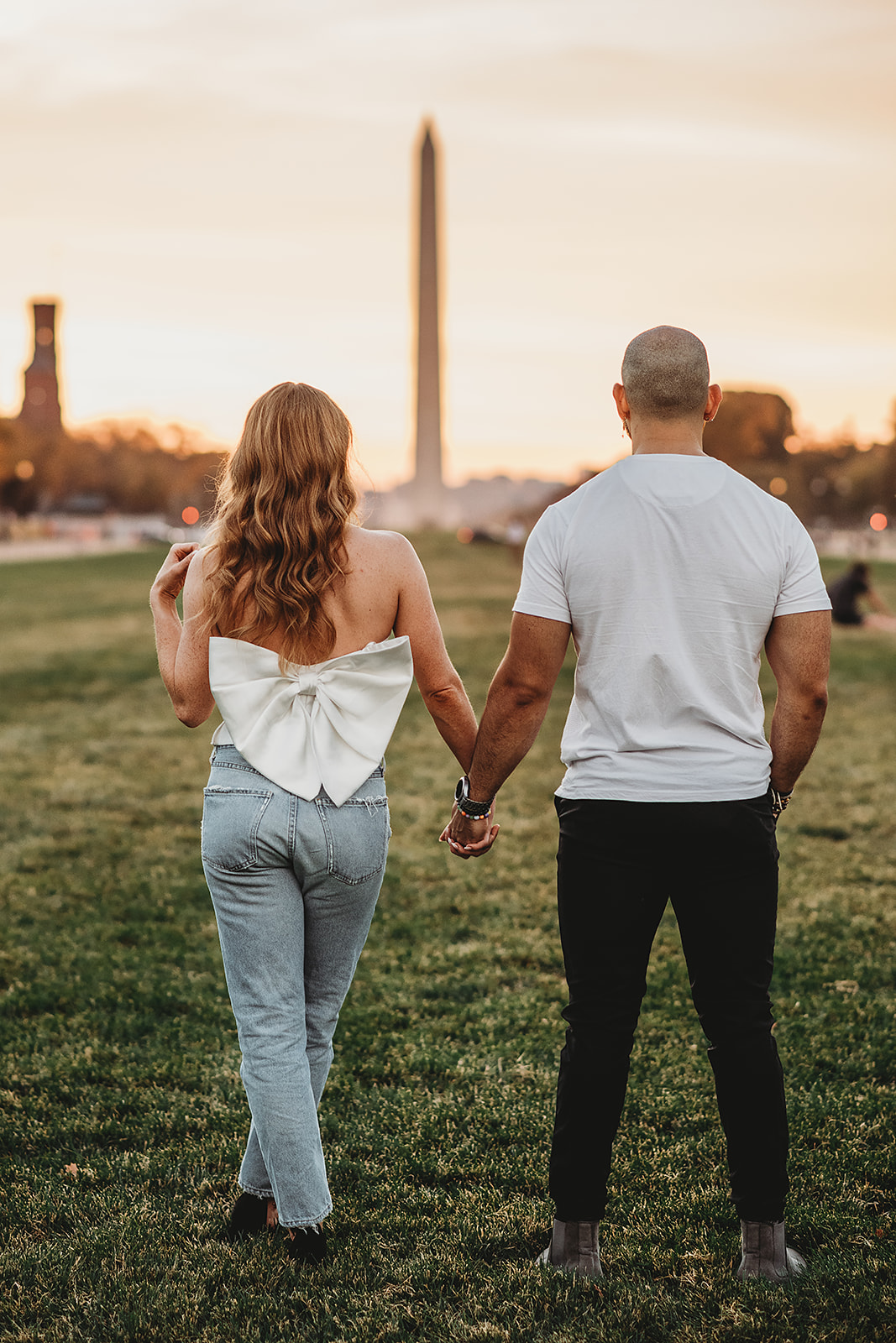 sunset engagement pictures with couple standing in the field in front of the Washington Monument and hold hands at sunset