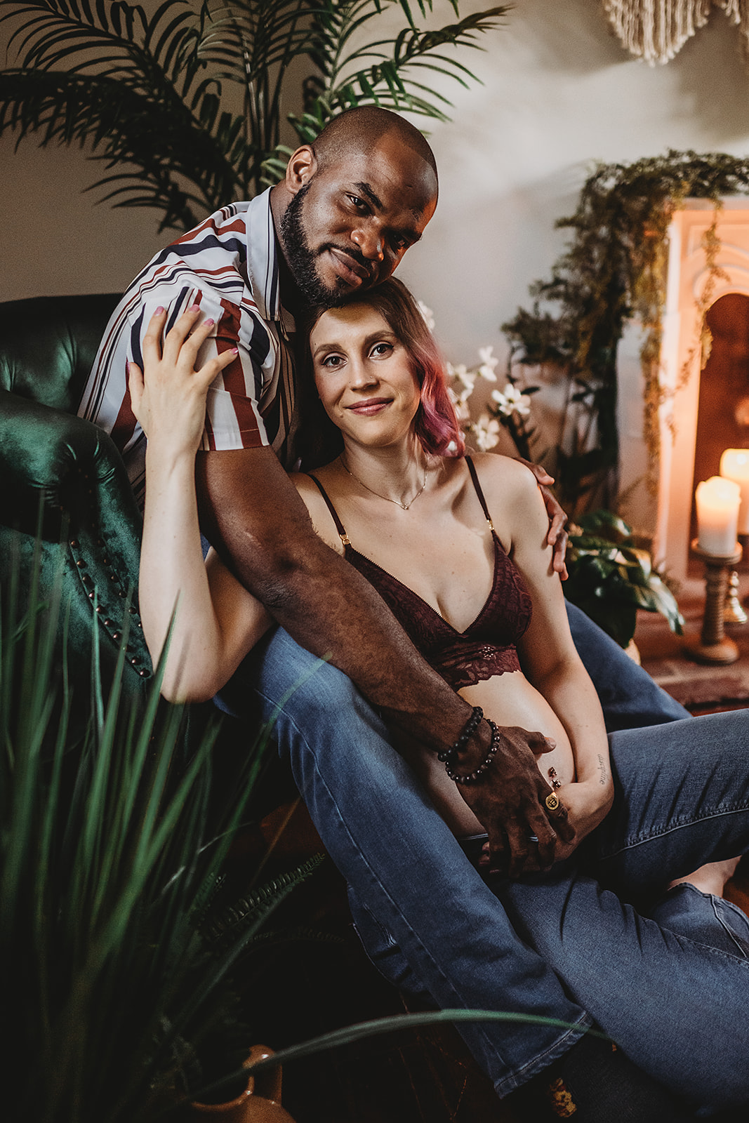 couples poses for maternity photos with man sitting on a green velvet couch and the pregnant woman sitting on the floor in front of him as he leans forward to hold the woman captures by Baltimore family photographer