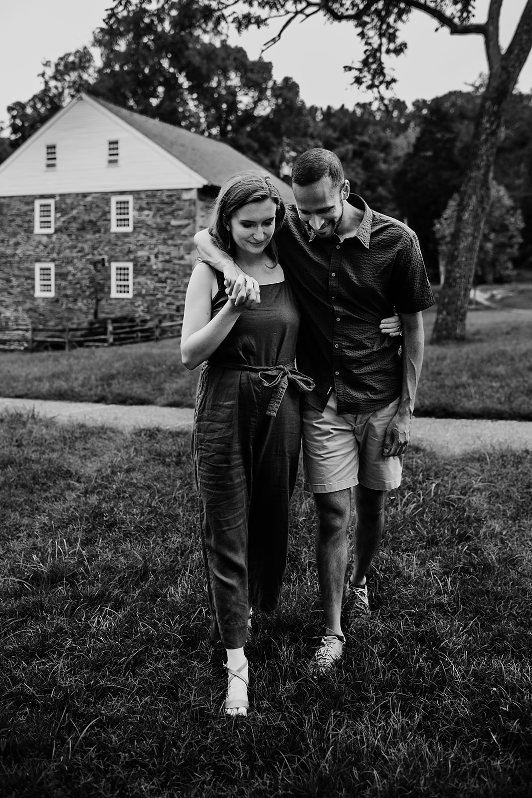 Baltimore photographer captures black-and-white engagement photo of a couple walking arm in arm through a grassy field in Washington, DC, with a historic stone building in the background