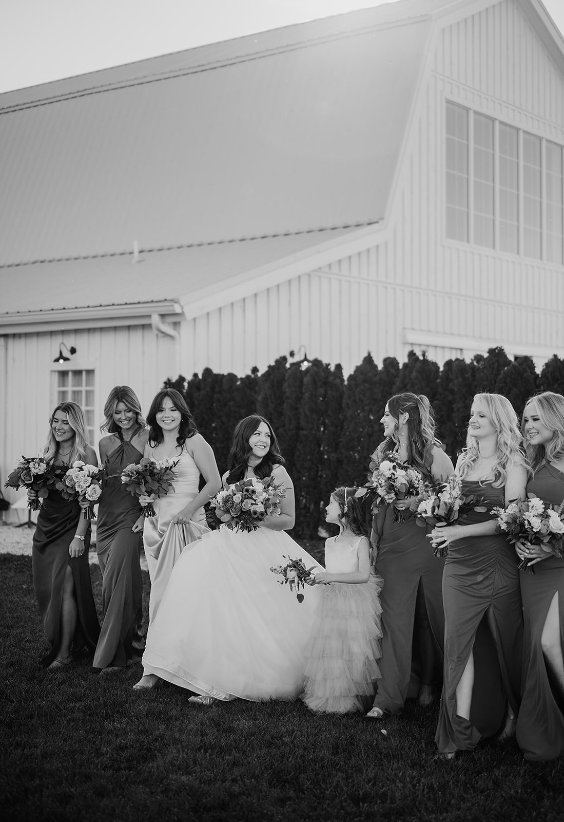 Bride surrounded by bridesmaids and a flower girl outside Breckenridge Barn, all holding floral bouquets and smiling, captured by a Baltimore wedding photographer.