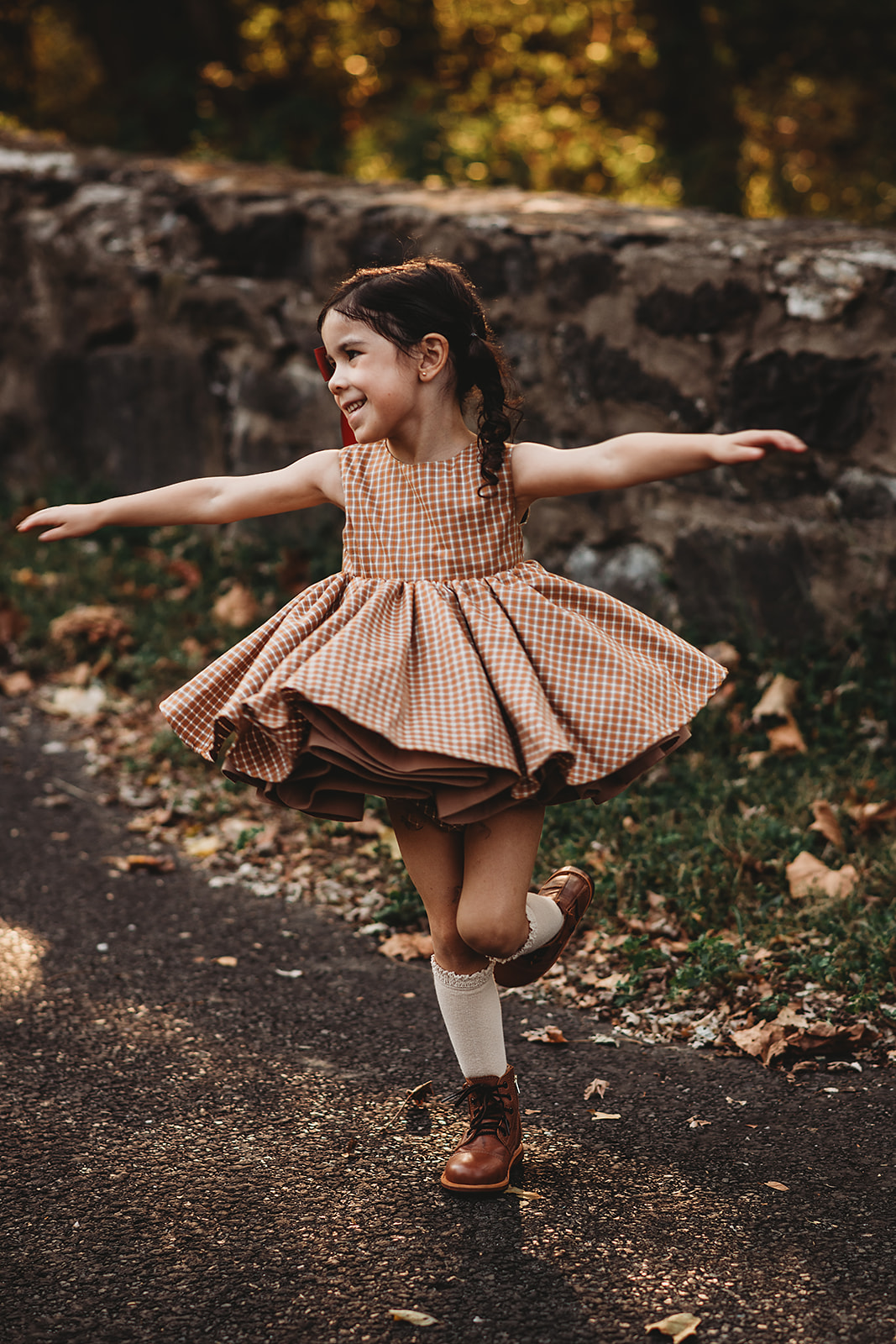 Young girl twirling joyfully in a gingham dress with a red ribbon in her hair during fall family photos by Baltimore family photographer.