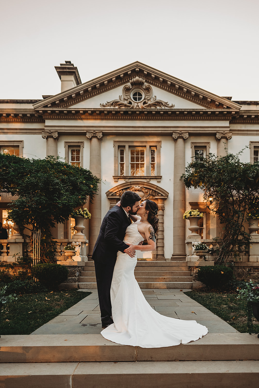 Bride and groom kissing in front of Liriodendron Mansion at sunset, with the historic architecture providing a romantic backdrop captured by a Baltimore wedding photographer.