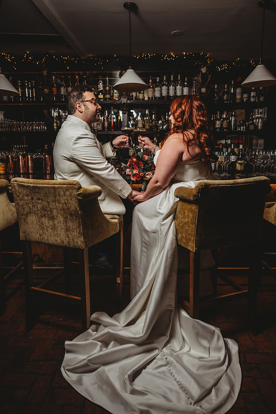Bride and groom toasting with cocktails at the Milton Inn’s dimly lit bar, surrounded by glassware and bottles, captured by a Baltimore wedding photographer for Great Gatsby wedding